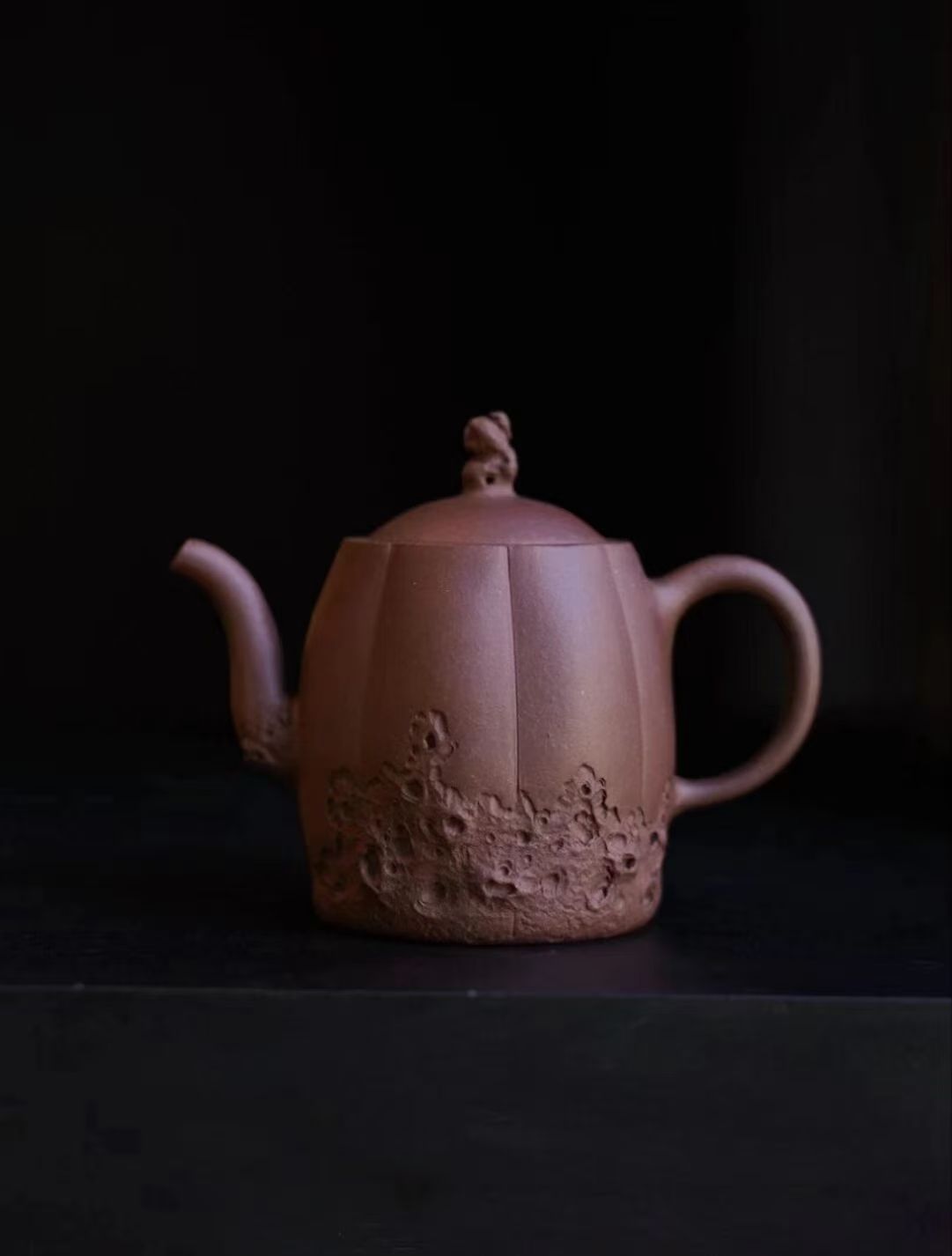 A melon-ribbed Yixing teapot with plum-blossom relief, lit against darkness
